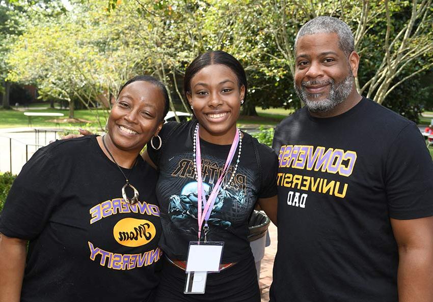 Prospective parents stand next to their child on the Converse campus smiling and wearing Converse University t-shirts.